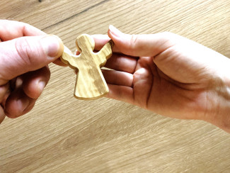 Zwei Hände von verschiedenen Personen, die gemeinsam einen Holzengel halten